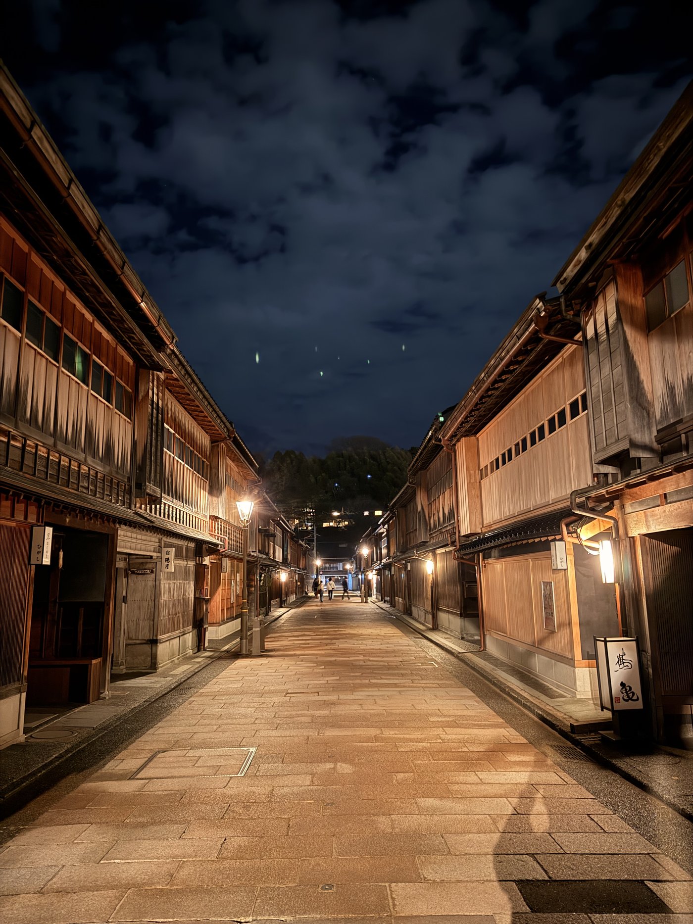 Higashi Chaya District after dark: lantern-lit wooden teahouses and stone paving — 夜のひがし茶屋街。灯りのともる格子戸の茶屋建築と石畳。